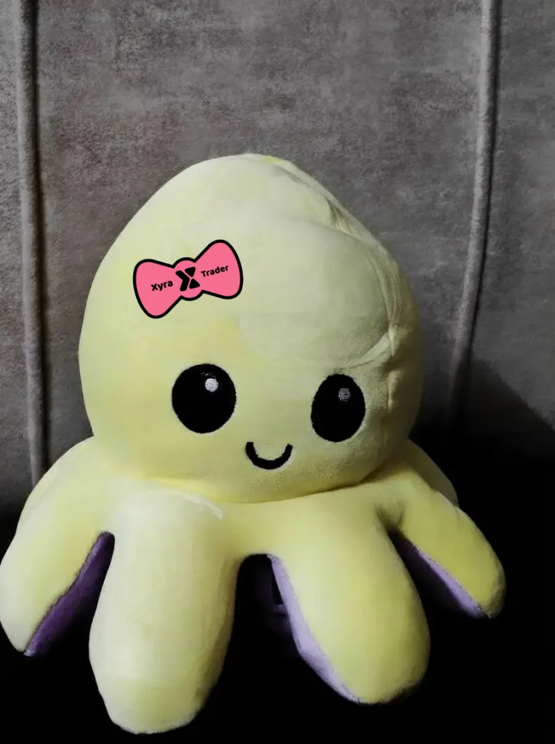 Photograph of the yellow reversible octopus plushie wearing the pink Xyra Trader bow